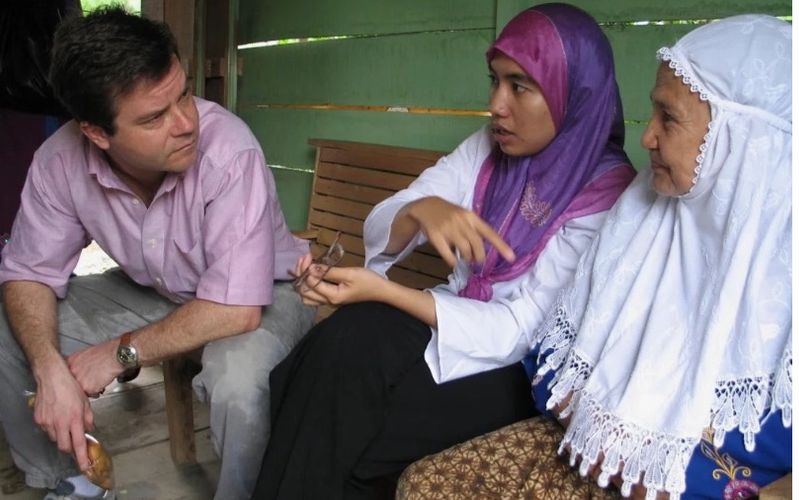 Alex Counts speaks intently with two women wearing traditional dress.